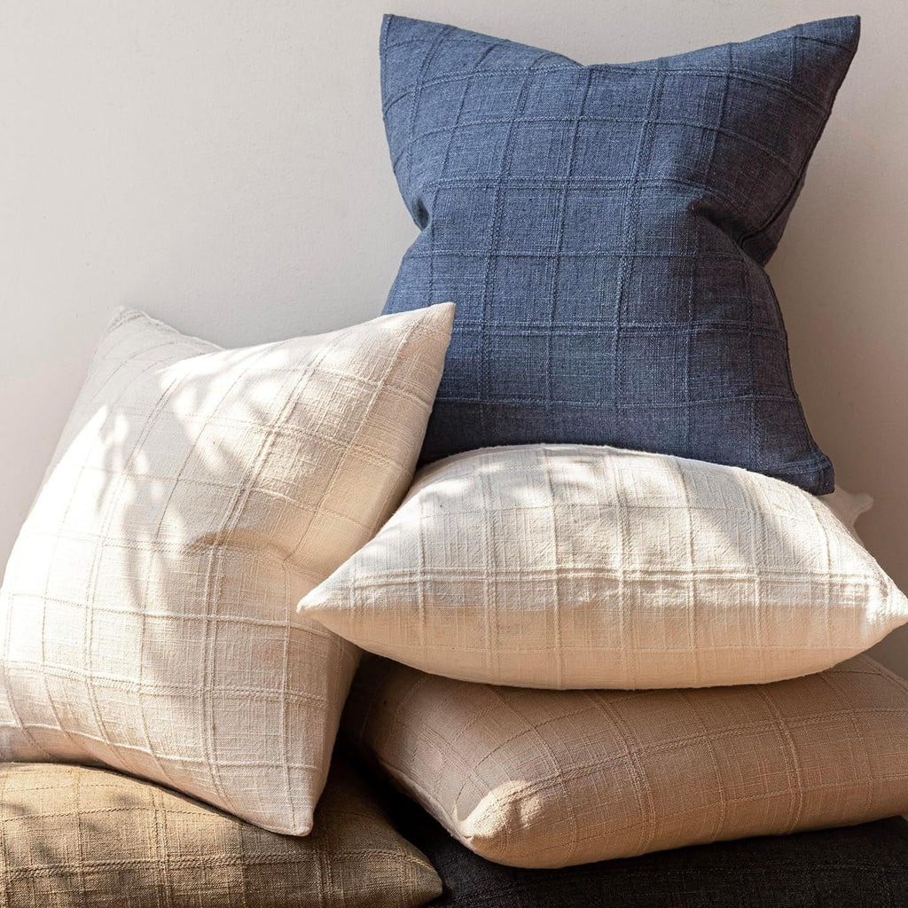 Stack of plaid pillows in various colors on a neutral background