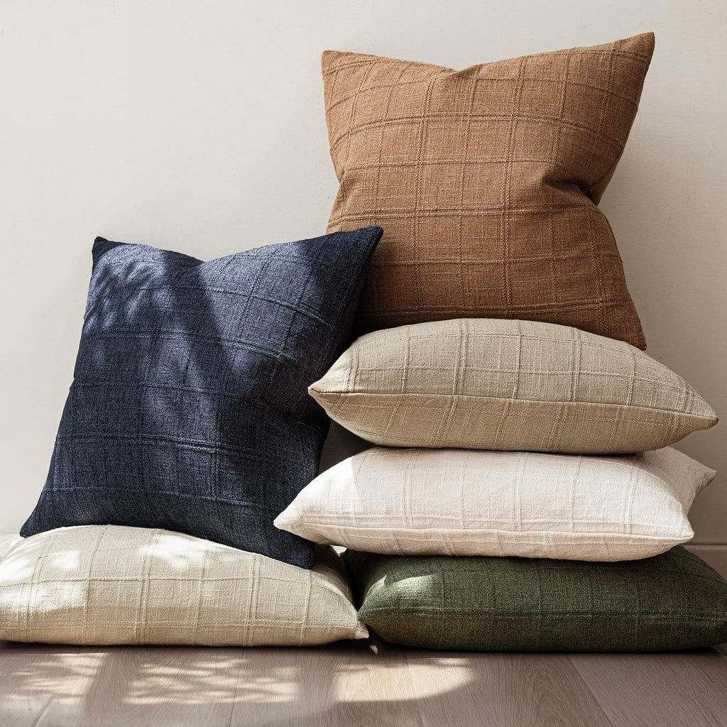 Stack of plaid pillows in various colors on a neutral background